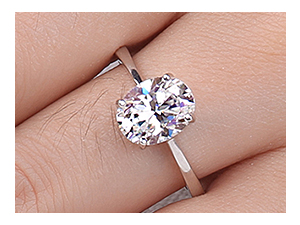 Primo piano di un anello in argento con una grande gemma rotonda e trasparente. Indossato su un dito su uno sfondo di pelle